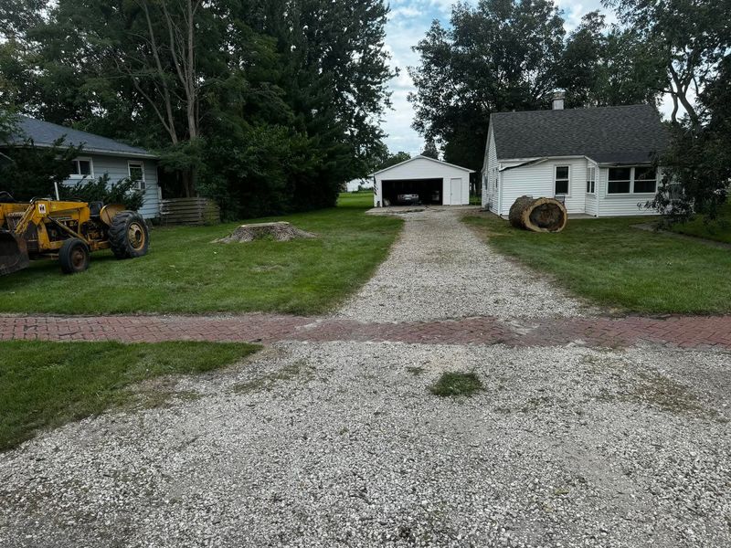 Open residential yard after tree removal and property cleanup, showing a ground-level stump and cleared driveway