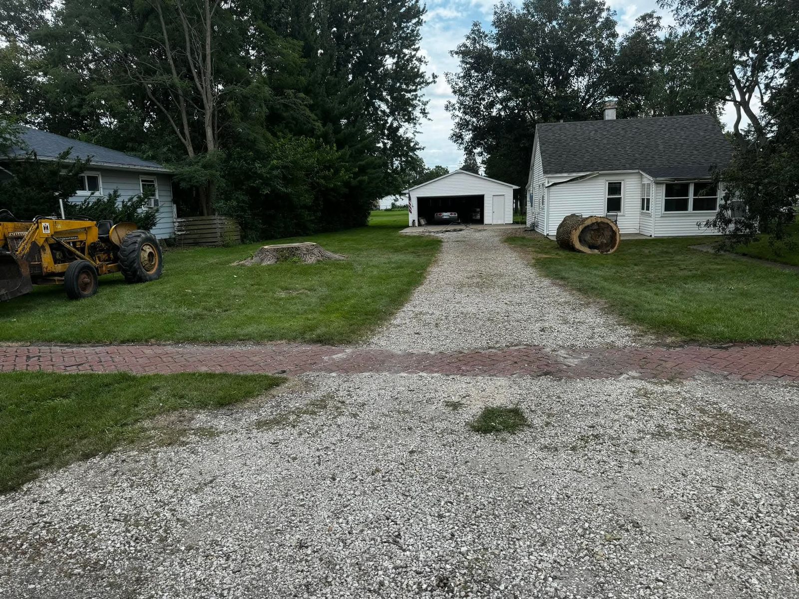 Cleared residential property in Galesburg, IL after tree removal and cleanup, with skid steer equipment and cut log rounds ready to haul